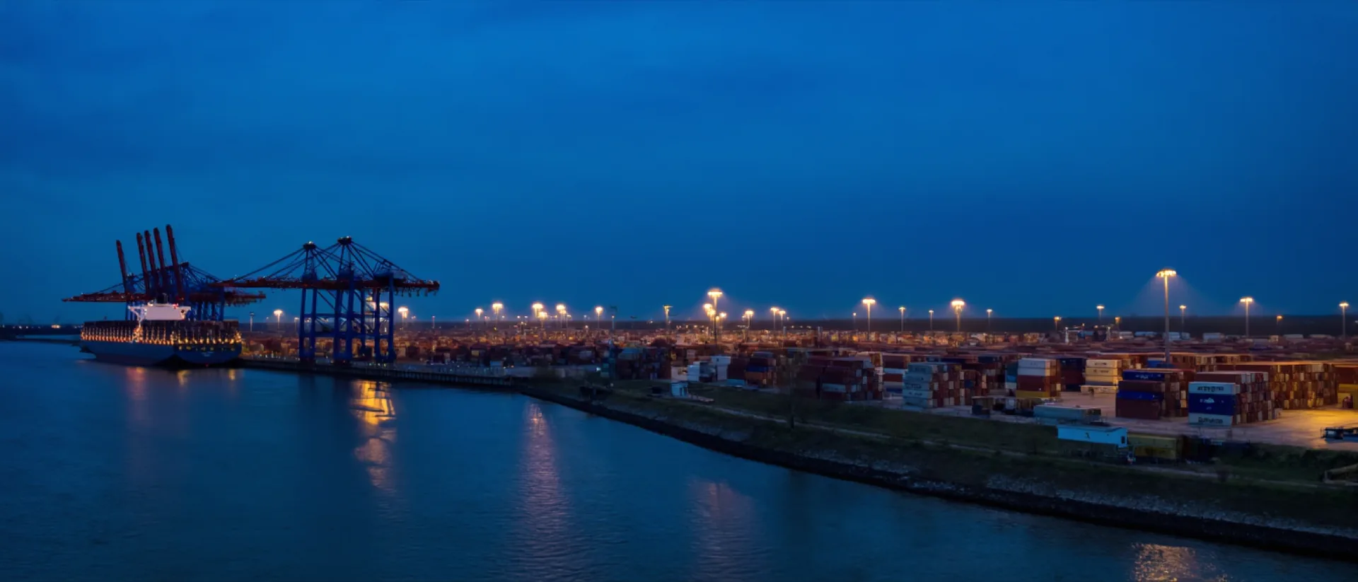 Container terminal on the Elbe at blue hour, a line of gantry cranes above a moored container vessel